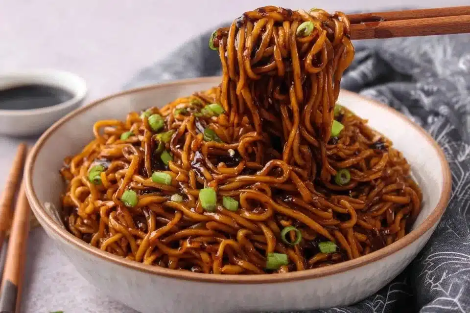Plate of sticky garlic chicken noodles topped with fresh herbs